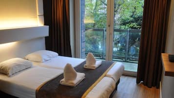Habitación de hotel con dos camas, balcón y vistas a árboles.