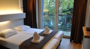Habitación de hotel con dos camas, balcón y vistas a árboles.