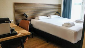 A hotel room with a bed, a desk with a laptop, a chair, and a window with curtains.