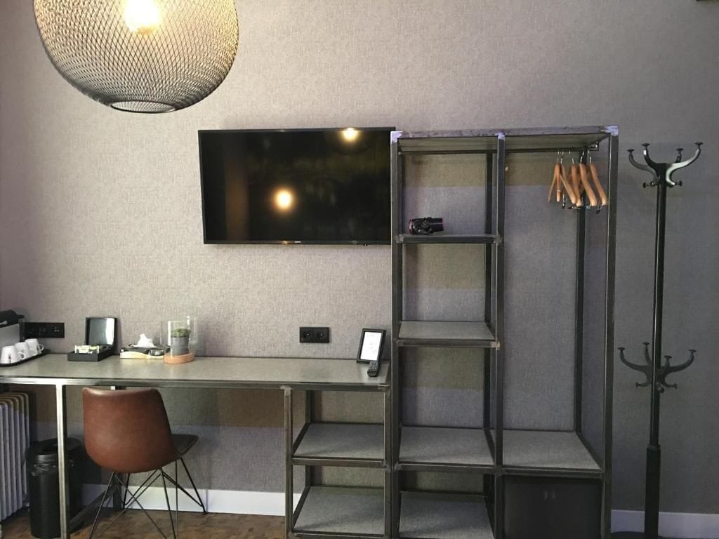 A modern room with a desk, a television mounted on the wall, and a metal shelving unit with hooks.