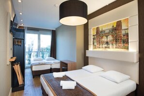Habitación de hotel con cama, escritorio, silla, ventana con vista a la ciudad y una obra de arte colgada en la pared.