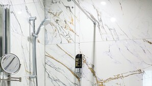 A bathroom with a marble wall, a shower, a sink, and a mirror.