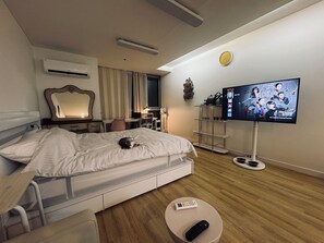 Hotellihuone, jossa on sänky, yöpöytä, televisio ja työpöytä tuolilla.