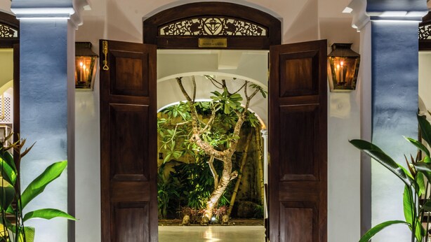 An entrance with a wooden door, a potted plant, and a bench. - Prince of Galle (Galle)