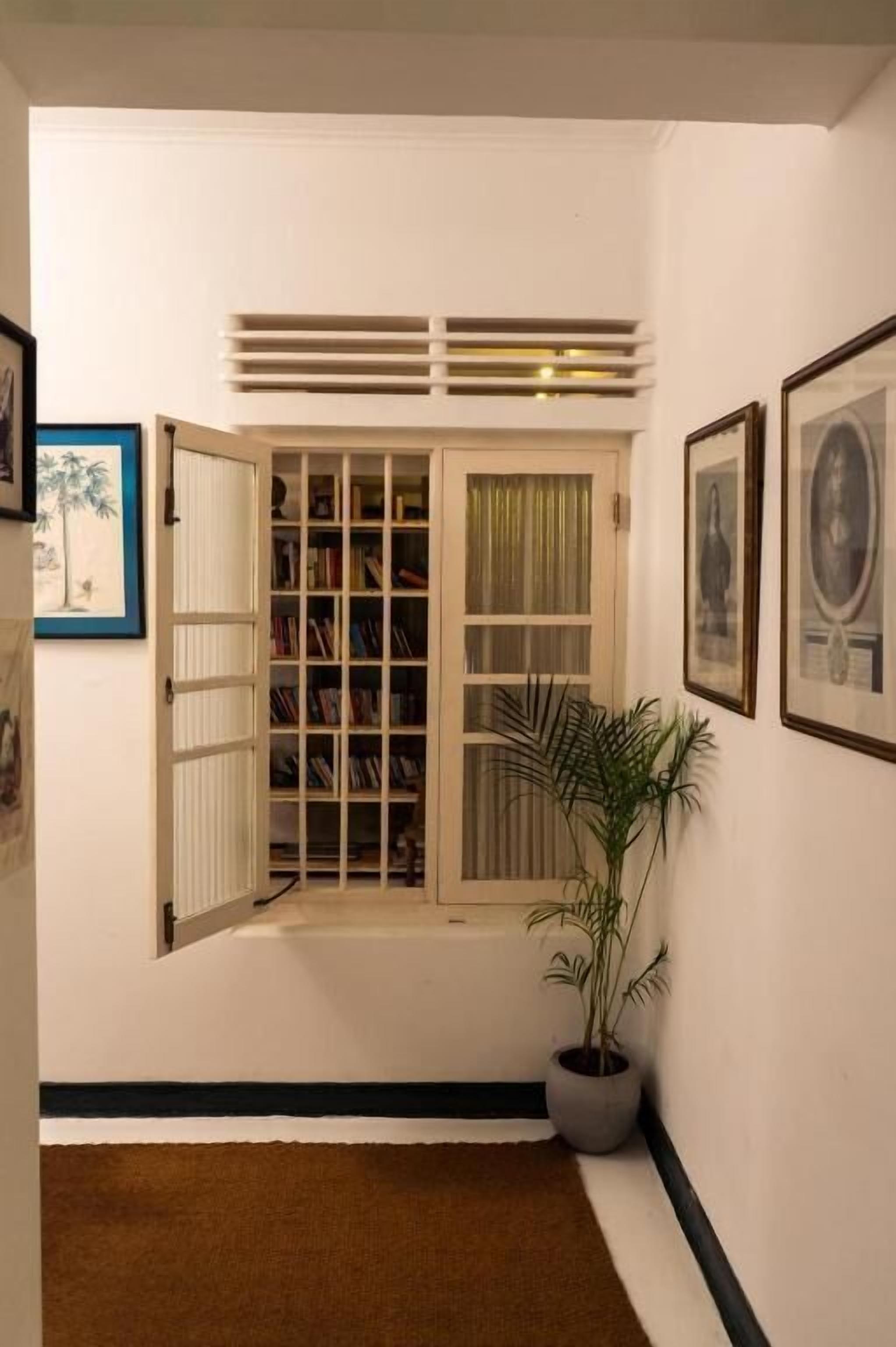 A hallway with a bookshelf, a potted plant, and framed pictures on the walls.