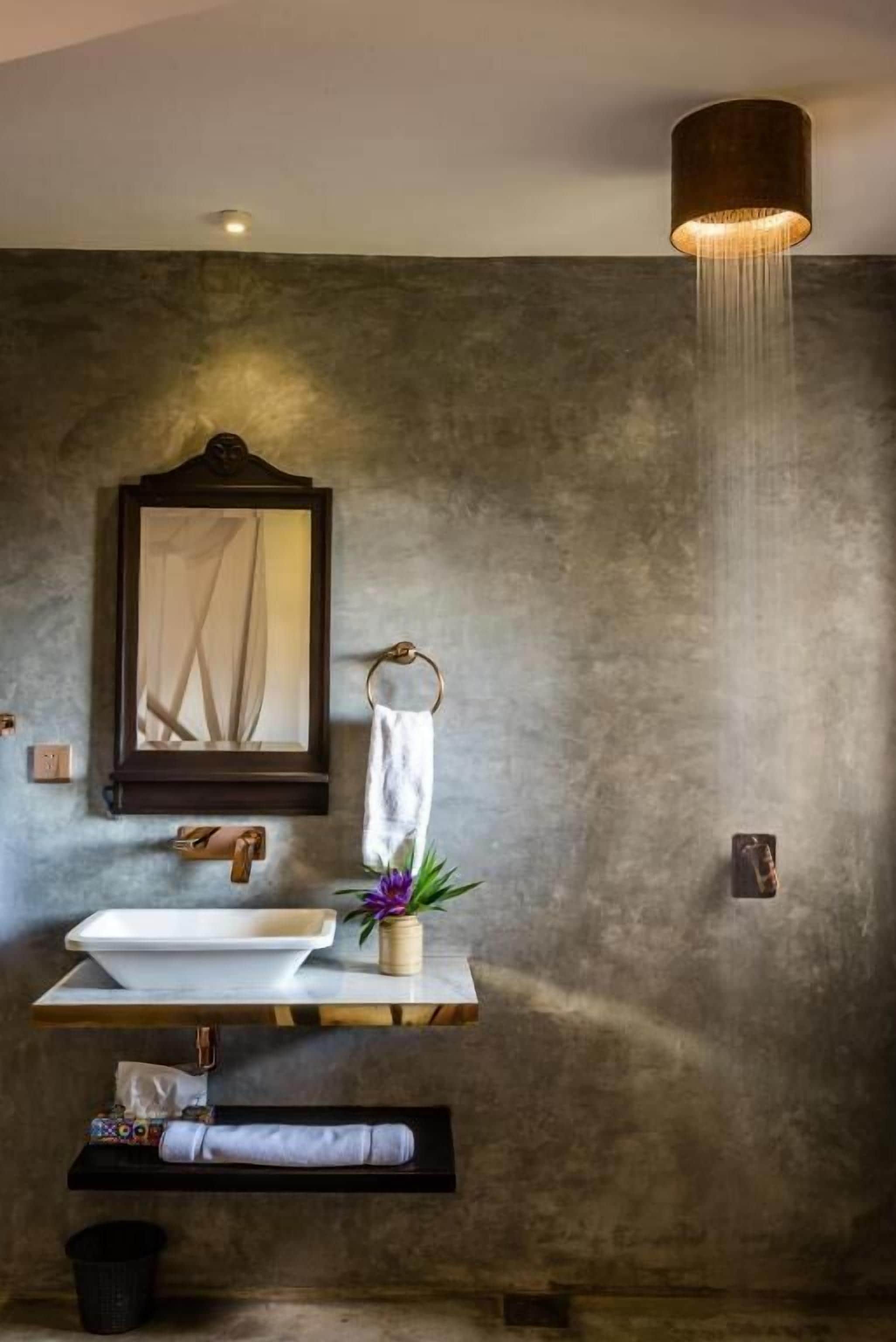 A bathroom with a large mirror, a towel rack, a sink with a vase of flowers, and a hanging light fixture.