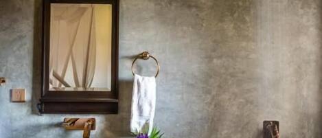 A bathroom with a large mirror, a towel rack, a sink with a vase of flowers, and a hanging light fixture.