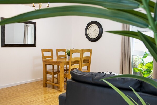 A room with a wooden dining table and chairs, a black sofa, a wall clock, and a window with curtains.