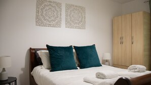 A neatly made bed with white bedding and teal pillows, a wooden wardrobe, and two wall decor pieces.