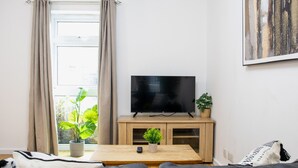A living room with a TV on a wooden stand, a coffee table, a sofa, and a window with curtains.