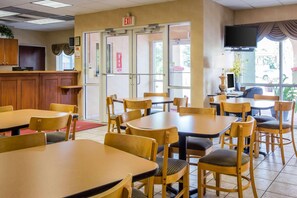 A restaurant with multiple tables and chairs, a counter with a computer, and a television mounted on the wall. - Econo Lodge Valdosta (Valdosta)