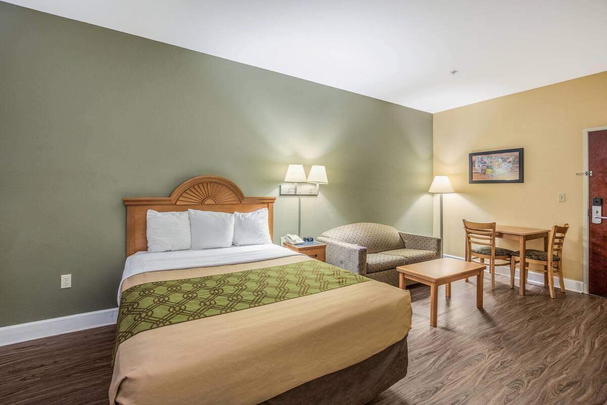 Ein Hotelzimmer mit Bett, Schreibtisch, Stuhl, Lampe und einem Bild an der Wand.
