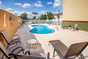 Un espace piscine avec des chaises longues et une petite table, le tout entouré d’une clôture.