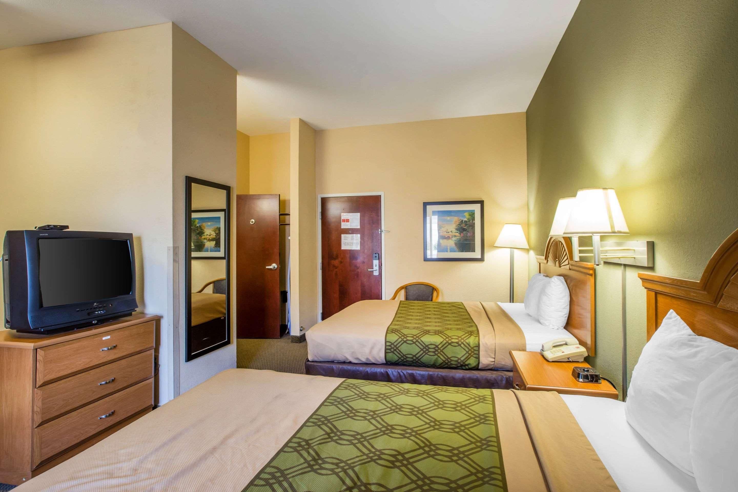 Quarto de hotel com duas camas, televisão, escrivaninha com abajur e uma cadeira.