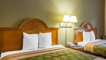 Quarto de hotel com duas camas, cada uma com cabeceira de madeira, roupa de cama branca e colcha verde com padrão. Há uma mesa de cabeceira com uma luminária e um telefone.