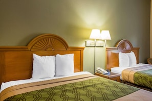 A hotel room with two beds, each with a wooden headboard, white bedding, and a green patterned bedspread. There is a nightstand with a lamp and a phone on it. - Econo Lodge Valdosta (Valdosta)