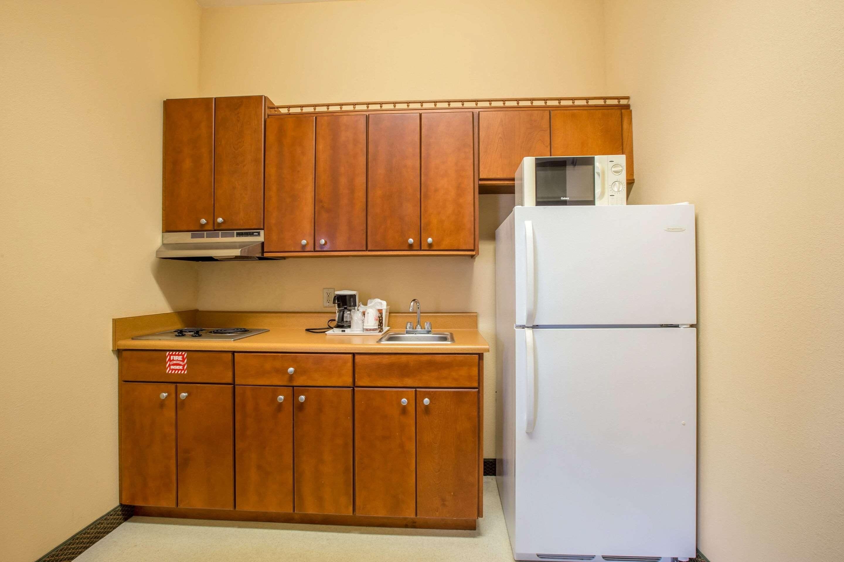 A compact kitchen with wooden cabinets, a white refrigerator, a microwave, and a coffee maker.
