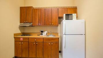A compact kitchen with wooden cabinets, a white refrigerator, a microwave, and a coffee maker.