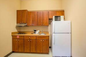 Une cuisine de taille réduite, dotée de meubles en bois, d’un réfrigérateur blanc, d’un four à micro-ondes et d’une machine à café.