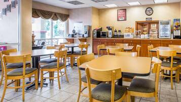 A restaurant with wooden tables and chairs, a kitchen area, and a clock on the wall.