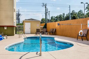 A swimming pool with a metal ladder, surrounded by a wooden fence, with chairs and a small building in the background. - Econo Lodge Valdosta (Valdosta)