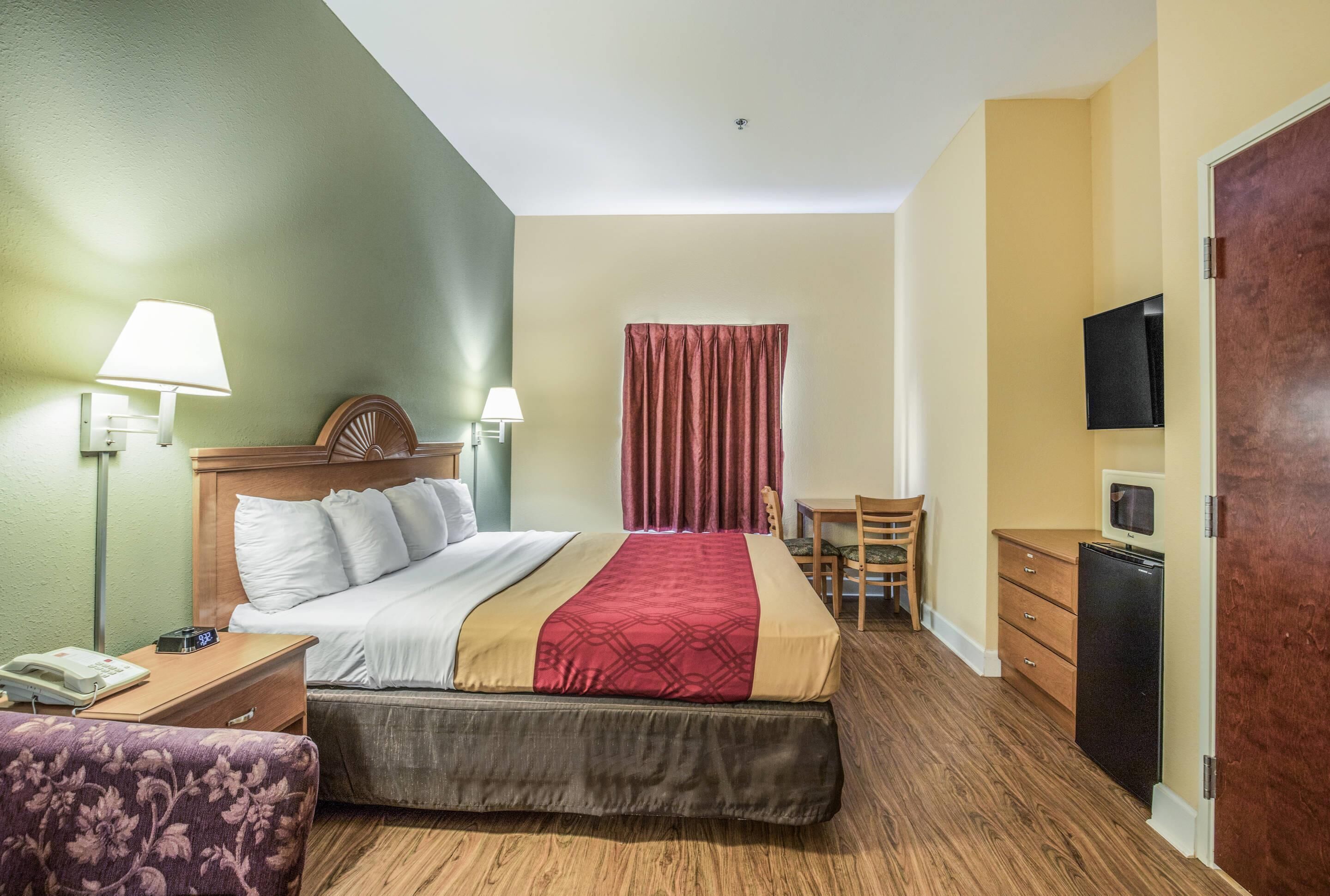 A hotel room with a bed, bedside tables, a desk, a chair, a television, and a wardrobe.