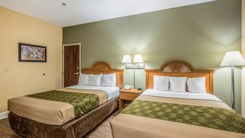 A hotel room with two beds, a wooden headboard, bedside lamps, a nightstand, and a framed picture on the wall.