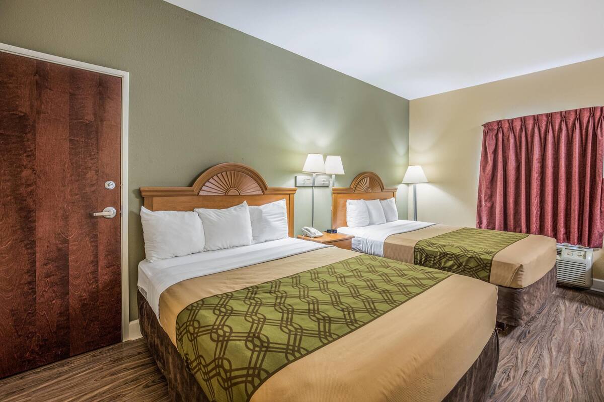 Ein Hotelzimmer mit zwei Betten, einer Holztür, einem Nachttisch mit Lampe und einem roten Vorhang.