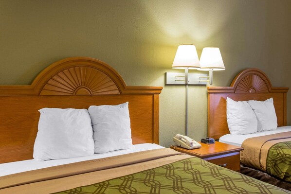 A hotel room with two beds, each with white bedding and a wooden headboard. There is a bedside table with a lamp and a telephone. - Econo Lodge Valdosta (Valdosta)