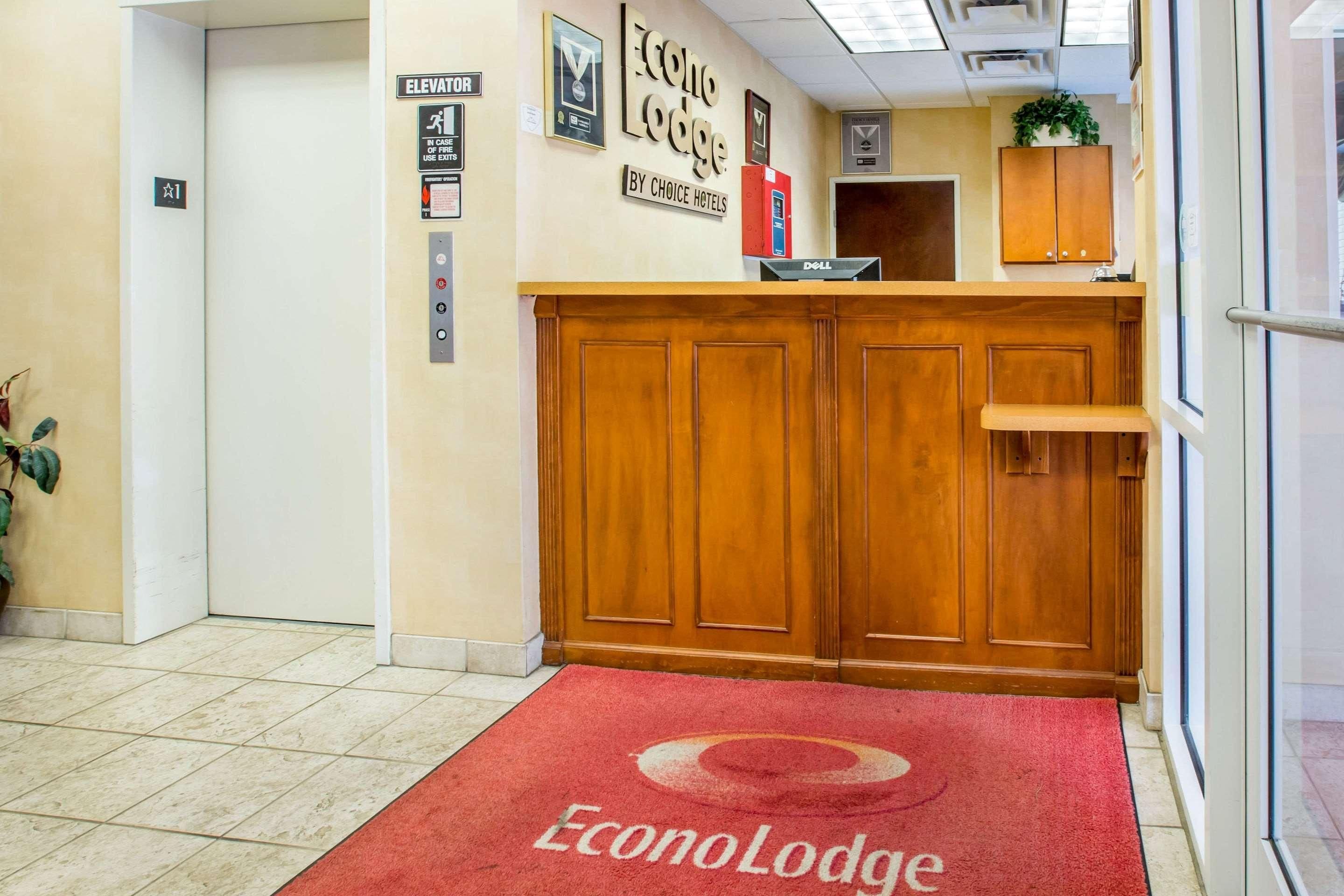 A hotel lobby with a red carpet, wooden reception desk, and an elevator sign.