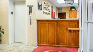 Un hall d’hôtel avec un tapis rouge, un comptoir d’accueil en bois et un panneau indiquant l’ascenseur.