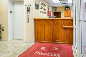 Un hall d’hôtel avec un tapis rouge, un comptoir d’accueil en bois et un panneau indiquant l’ascenseur.