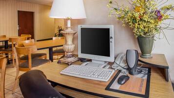 Et hotelværelse med skrivebord, computer, telefon og en vase med blomster.