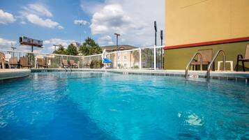 A swimming pool with a white fence, lounge chairs, and a building in the background.