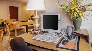 Quarto de hotel com escrivaninha, computador, telefone e um vaso com flores.