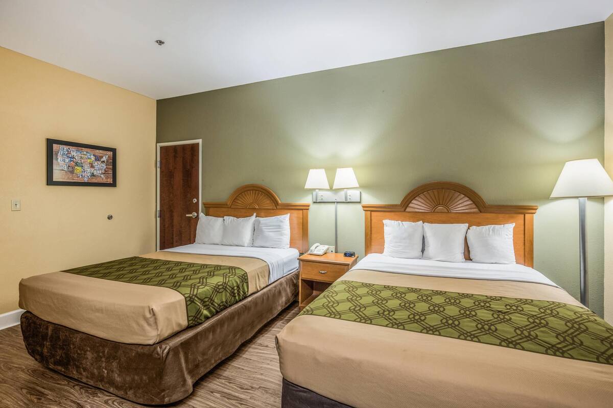 Ein Hotelzimmer mit zwei Betten, einem hölzernen Kopfteil, Nachttischlampen, einem Nachttisch und einem gerahmten Bild an der Wand.