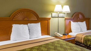 Quarto de hotel com duas camas, cada uma com roupa de cama branca e cabeceira de madeira. Há uma mesa de cabeceira com uma luminária e um telefone.