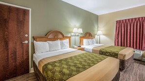 Ein Hotelzimmer mit zwei Betten, einer Holztür, einem Nachttisch mit Lampe und einem roten Vorhang.