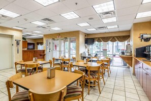 Un restaurant doté de nombreuses tables et chaises, d’un ascenseur et d’un téléviseur fixé au mur.