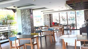 A restaurant interior with multiple tables and chairs, stone accents on the walls, and a view of the outside through large windows. - SERRA HOTEL BATAM (Batam)