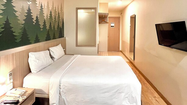 A hotel room with a bed, a nightstand, a TV mounted on the wall, and a mural of trees on the wall. - SERRA HOTEL BATAM (Batam)