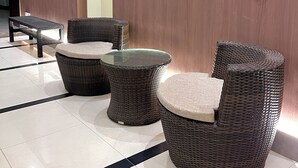A modern lounge area with wicker furniture, including a round table and two chairs, against a wooden wall. - SERRA HOTEL BATAM (Batam)