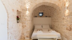 A stone-walled bedroom with a bed, a nightstand, and a small table. - Trulli Scacciapensieri con Piscina (Ceglie Messapica)