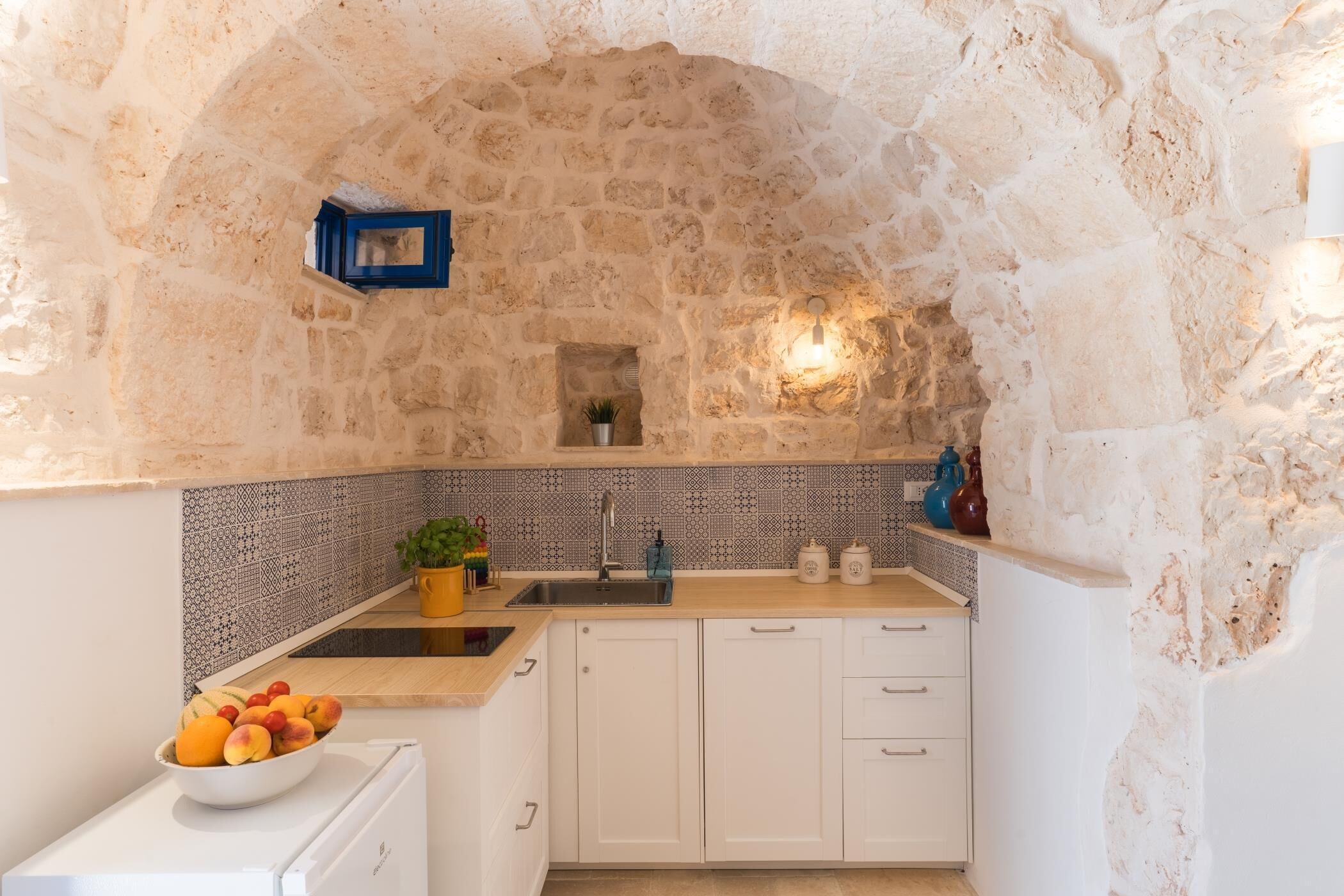A kitchen with stone walls, a tiled backsplash, and white cabinetry.