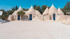 A row of stone buildings with conical roofs, each with a blue door, set against a clear blue sky. - Trulli Scacciapensieri con Piscina (Ceglie Messapica)