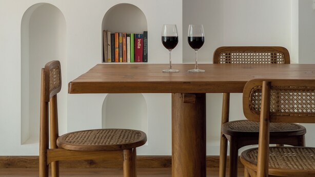 Un comedor con una mesa de madera, sillas de mimbre y estanterías llenas de libros y objetos decorativos.