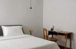 A bedroom with a bed, a desk, a chair, a lamp, and a vase with flowers. - Bungalow 157 (New Delhi)