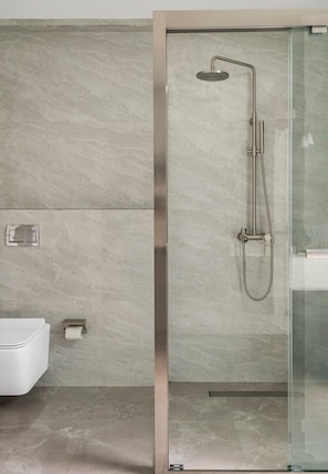 A modern bathroom with a glass-enclosed shower, a toilet, and a paper towel dispenser. - Bungalow 157 (New Delhi)