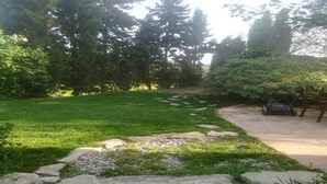 A well-maintained grassy area with a stone border, surrounded by tall trees and a wooden structure. - Detached rural 19th century country house. (Calonge de Segarra)
