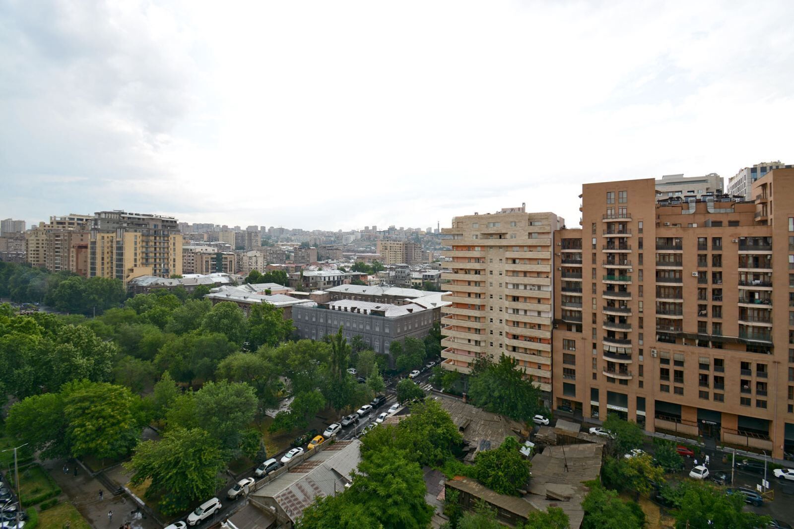 A cityscape with high-rise buildings, a mix of residential and commercial structures, and a dense tree line in the foreground.